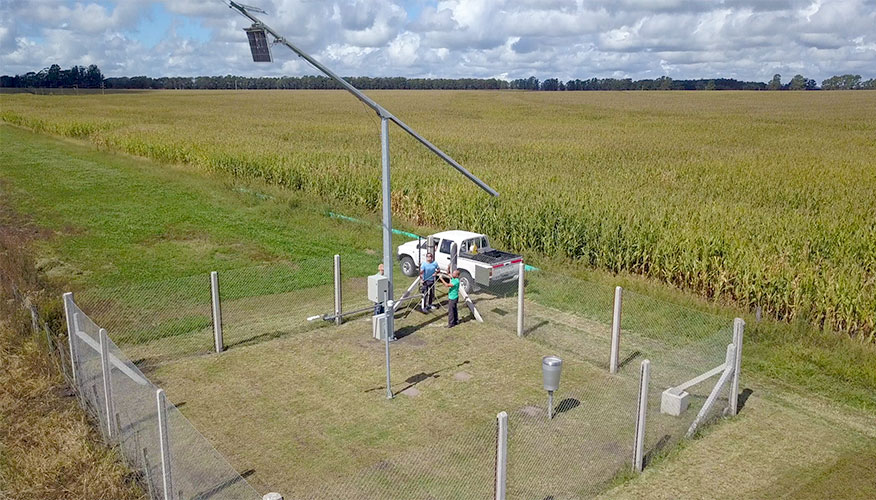 Monitoring station in Argentina located in a field seen from above; two people are working to readjust the equipment. A pick-up truck is parked nearby.