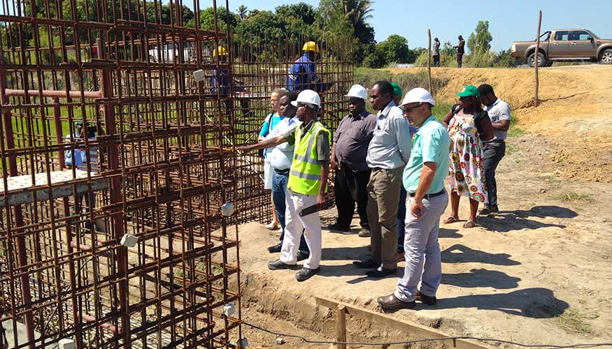 Group of people gathered outdoors at a building site in Mali, discussing the work. Builders are visible in the background.