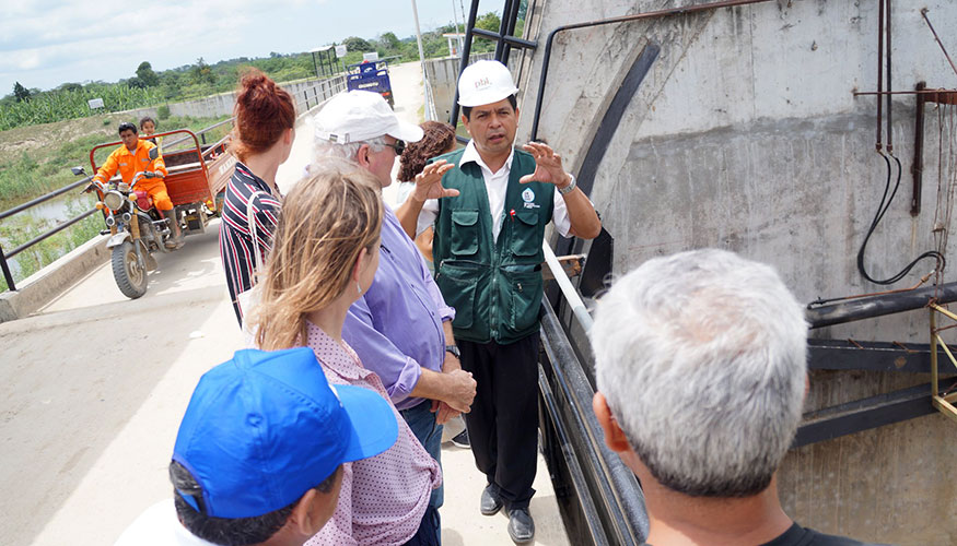 People gathered around a man in a hard hat, who is explaning something about the technical installation behind him.