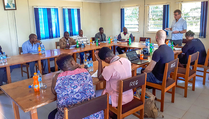 Meeting room with people seated at tables for a traning session. One man is stood, giving a presentation.