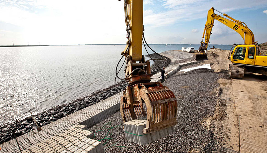 Large excavators placing concrete blocks on a dyke at the edge of water in the Netherlands..