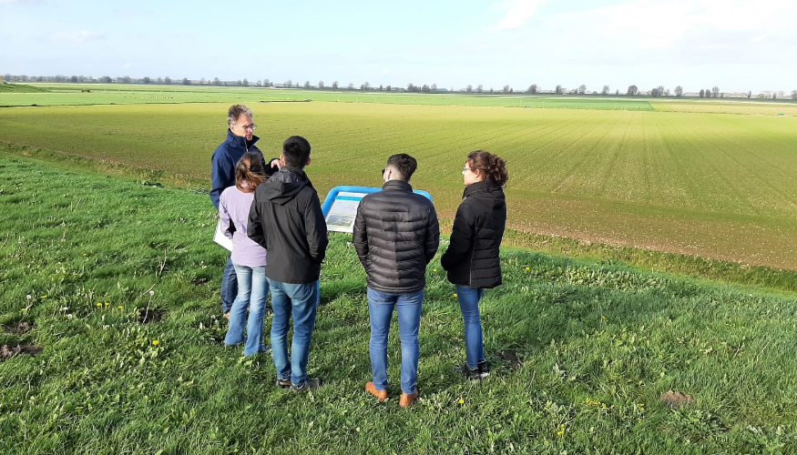 5 are standing in front of a sign next to a meadow.