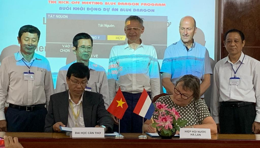 2 people are signing a paper, while 5 persons are standing in the back.