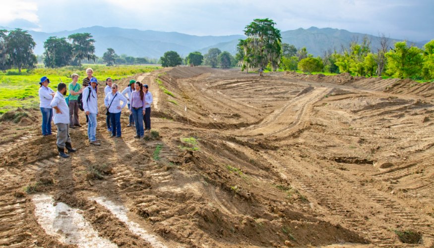 A group of people are standing in the middle of an excavation. In the background there are mountains.