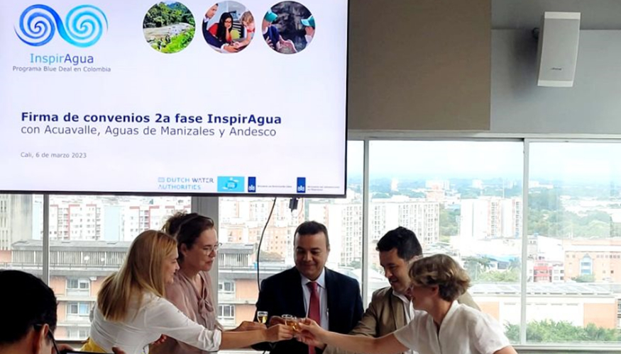 Five people are making a toast in front of a large screen with the logo of InspirAgua on it.