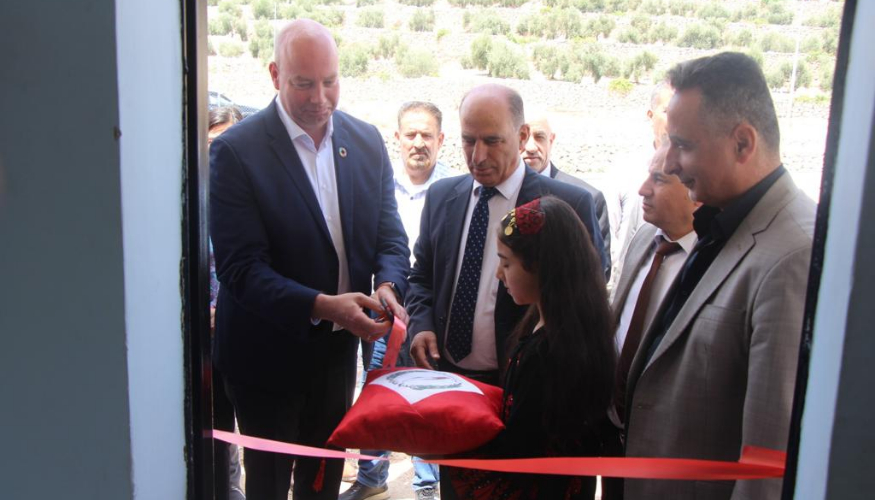 A man is standing next to a girl who holds a red pillow in front of a red large ribbon