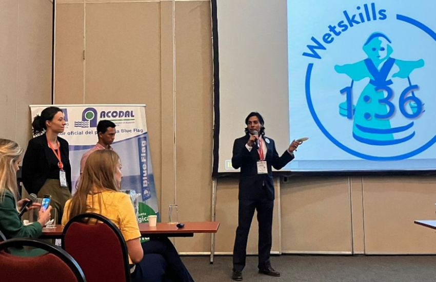 A man is presenting something, next to a screen with the logo of Wetskills on it