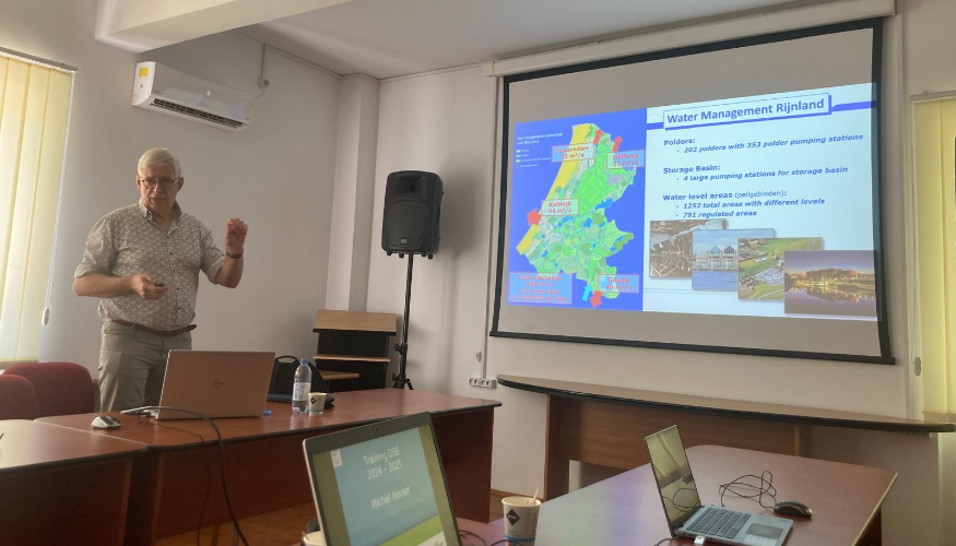 A man is standing next to a screen, giving a presentation