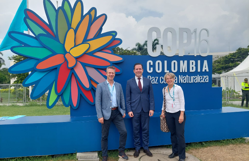 3 people are standing in front of the COP 16 sign.