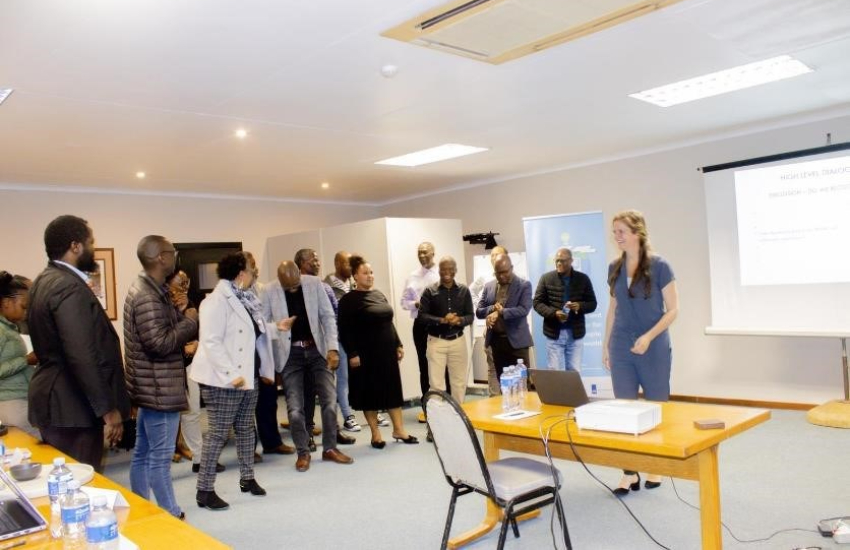 A group of people is standing on the side, looking at a presentation on a screen.