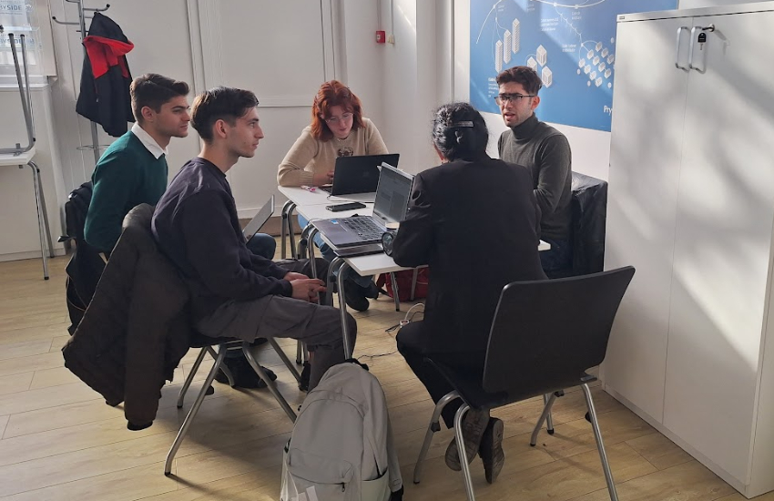 A group of 5 young people is sitting around a table, discussing something.